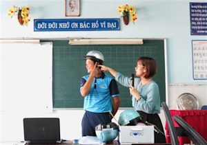 AIP Foundation Program Assistant, Nguyen Thi Huong Giang, and a teacher demonstrate the three steps to properly wearing a helmet.